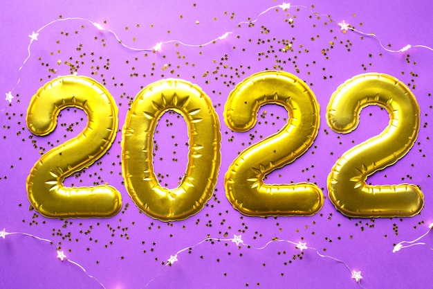 Happy new year- golden numbers 2022 on a purple background with sequins, stars, glitter, lights of garlands. greetings, postcard. calendar, cover.