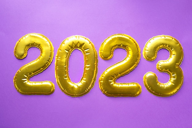 새해 복 많이 받으세요- 금색 숫자 2023은 장식 조각, 별, 반짝이, 화환 조명이 있는 보라색 배경에 있습니다. 인사말, 엽서입니다. 달력, 표지.
