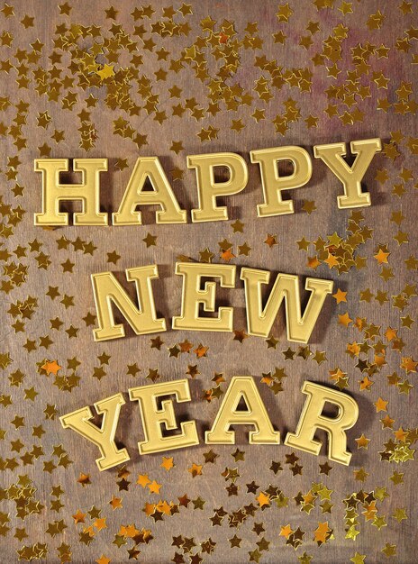 Photo happy new year golden text and golden stars on a wooden background