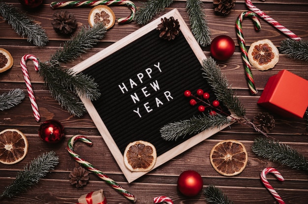 新年の装飾、モミの枝、コーン、ボール、キャラメルの杖のレターボードに新年あけましておめでとうございますの碑文。上面図。クリスマスカード。