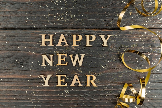 写真 木製の文字で作られた新年あけましておめでとうございます碑文は、新年のお祝いのグリーティング カード コピー スペース wih 木製の背景にお祭りの黄金蛇紋岩を装飾