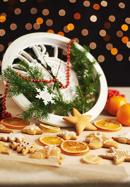 Foto felice anno nuovo a mezzanotte, vecchio orologio in legno con luci natalizie e rami di abete. cucinare e decorare biscotti di panpepato di natale e fette di arancia fritte