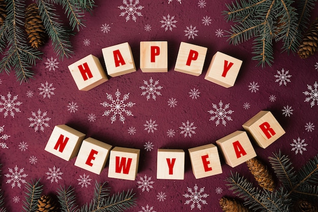 Happy new year text sign on wooden cubes with frame of christmas tree branch and cones on red backgr...