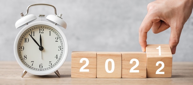 Happy new year with vintage alarm clock and hand flipping 2021 change to 2022 block. christmas, new start, resolution, countdown, goals, plan, action and motivation concept