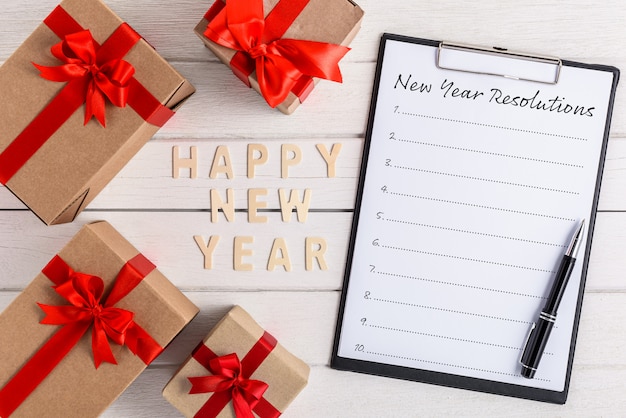 HAPPY NEW YEAR Wood and New Year's Resolutions List written on clipboard with gift box