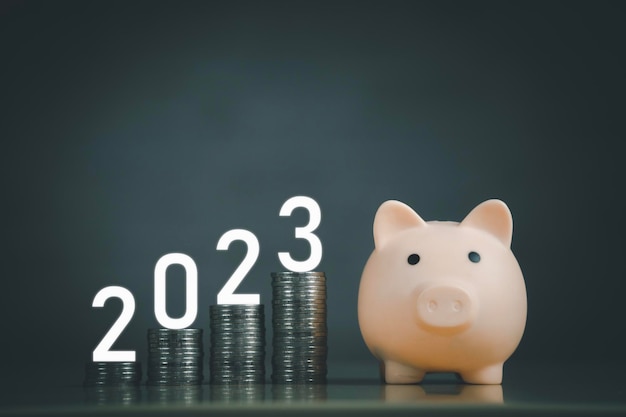 Happy new year wooden cube year 2023 on top stack rows of coins and pink piggy bank with dark background and copy space saving money and financial plan concept for investment in new year 2023