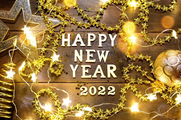새해 복 많이 받으세요 나무 글자와 숫자 2022는 장식 조각, 별, 반짝이, 화환 조명이 있는 축제 배경입니다. 인사말, 엽서입니다. 캘린더, 커버