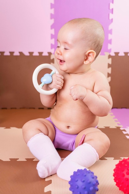 Happy newborn baby sitting on the floor with a toy