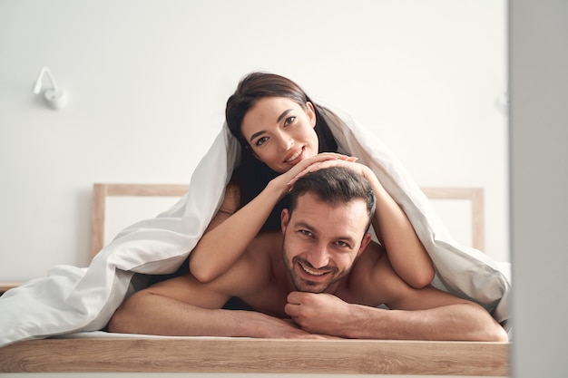 Foto felice coppia di sposi che si diverte a letto sotto le coperte al mattino