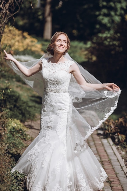 Happy newlywed bride swirling in white wedding dress in romantic garden with floral archway