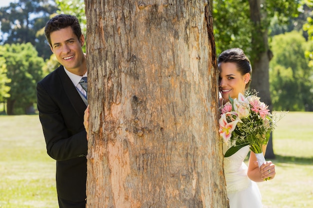 公園の木の幹の後ろに幸せな新婚カップル