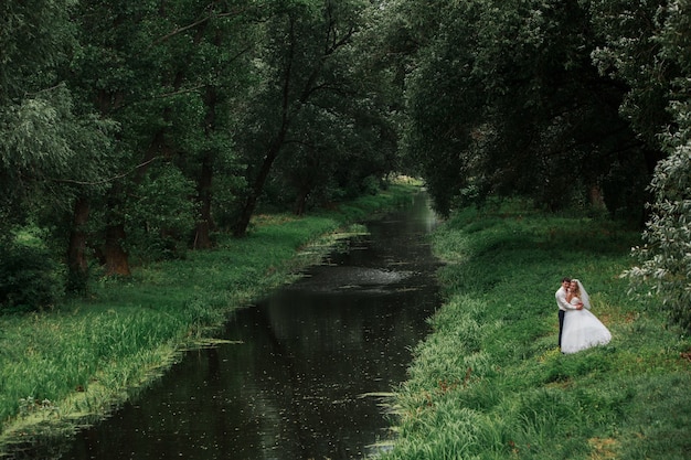 happy newlyweds outdoors near river. bride and groom kissing outdoor on green  park