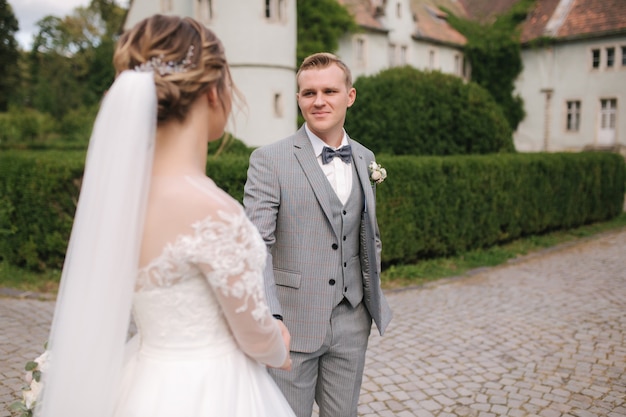 Happy newlyweds walking near the big castle. Groom and bride outside on their wedding day