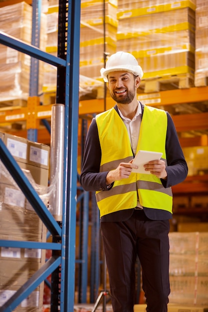 Happy nice man wearing professional uniform while doing the revision of the warehouse inventory