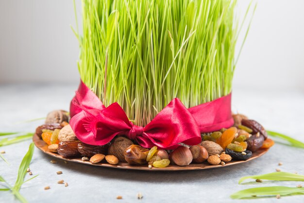 Happy Nowruz holiday wall. Celebrating  various dried fruits, nuts, seeds, light wall with green grass wheat, copy space top view