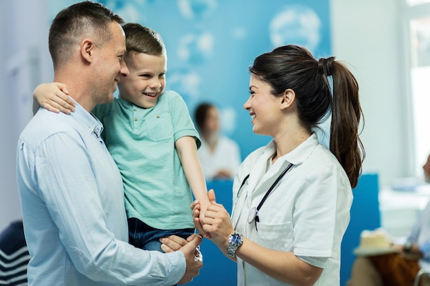 Happy nurse holding hands and communicating with small boy who came with father to a clinic