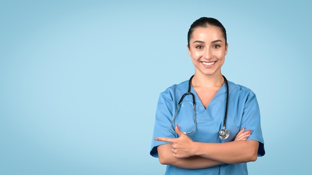 Happy nurse pointing left at free space wearing blue scrubs