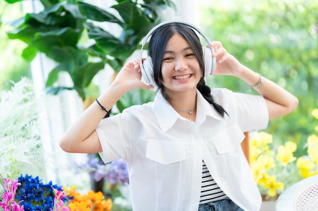 사진 귀여운 미소의 행복한 아시아의 매력적인 젊은 귀여운 작은 소녀는  ⁇ 색 무선 헤드폰을 착용하고 음악을 듣고 카페에서 좋아하는 오디오를 즐기고 카페에서 휴가를 보내고 있습니다.