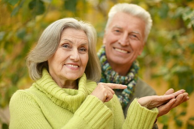 Happy old couple posing at autumn park,woman shows something by her finger