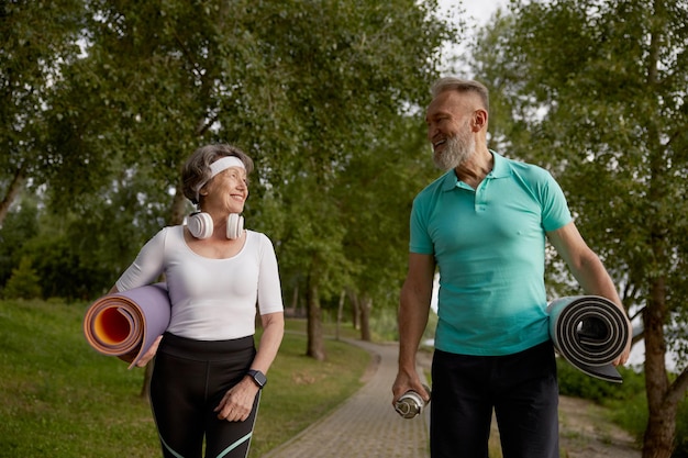 Happy old friends with sports mat having fun together before or after sport workout outdoors in green summer park