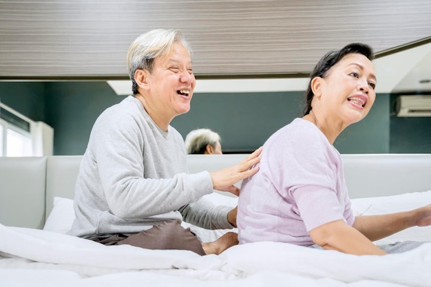 Happy old man massage backbone of his wife on bed