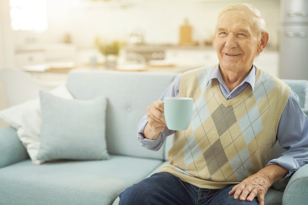 Happy old man resting on sofa with cup of tea