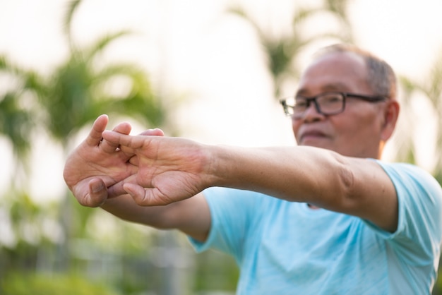 A happy old man stretching arm before outdoor exercise in a park