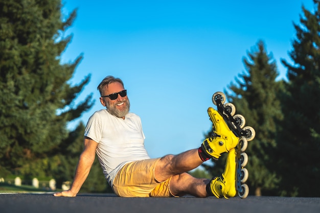 The happy old man with a roller skates sitting on the asphalt