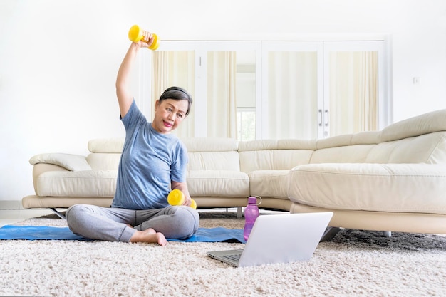 Happy old woman exercise with dumbbells on laptop