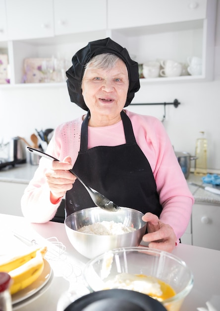 Happy old woman making pancakes in the kitchen