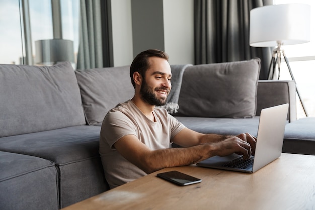 Photo a happy optimistic young man indoors at home using laptop computer.