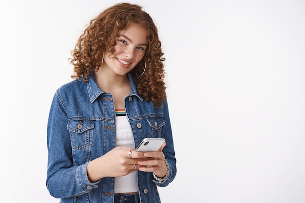 Happy outgoing stylish ginger adolescent girl curly-haired pimples holding smartphone playing phone game use funny app look you devious joyfully smiling messaging talking you same time