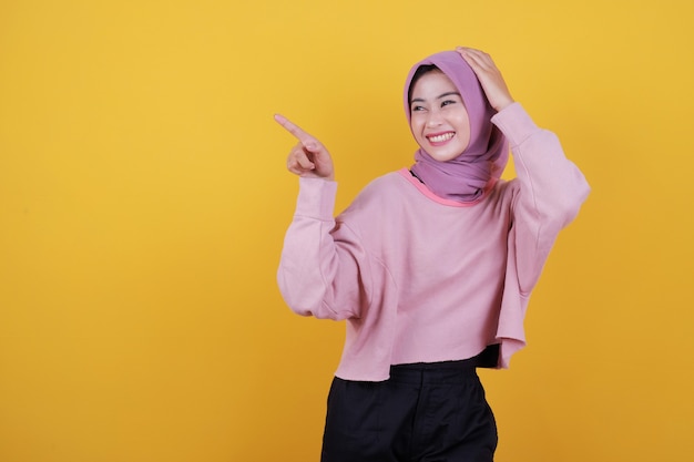 Happy overjoyed beautiful woman pointing something wearing soft pink T shirt, ho;ding her head