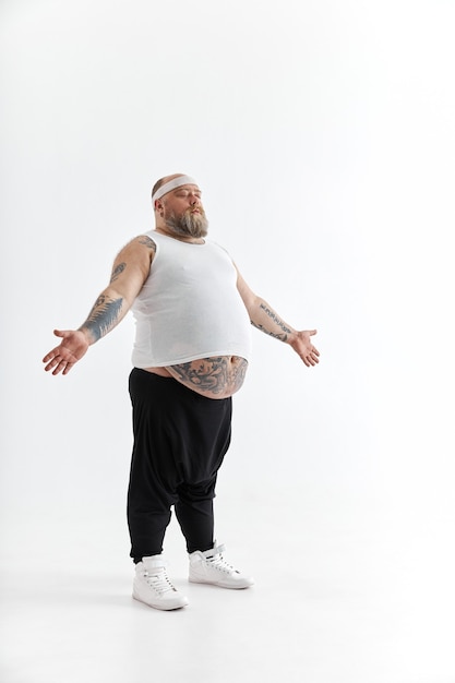 Photo happy overweight man with big belly and tattoos in sports wear posing on white background