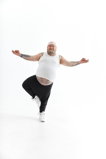 Happy overweight man with big belly and tattoos in sports wear posing on white background