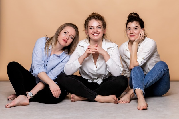 Happy and overweight multicultural women in bras isolated on beige. Diverse Beauty. Three Multiethnic Ladies Wrapped In Bath Towels Posing Smiling  On beige wall. 