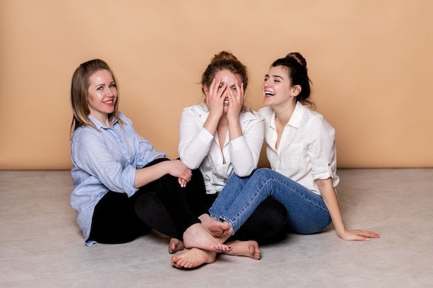 Happy and overweight multicultural women in bras isolated on beige. Diverse Beauty. Three Multiethnic Ladies Wrapped In Bath Towels Posing Smiling  On beige wall. 
