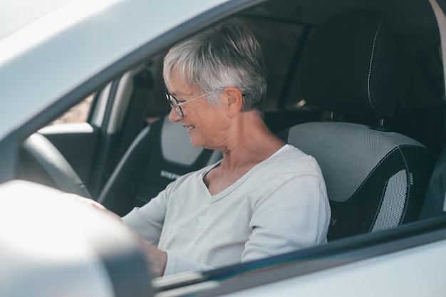 幸せな所有者ハンサムな成熟した女性は、彼の新しく購入した車でリラックスして座って、嬉しそうに笑っている道路を見ています。