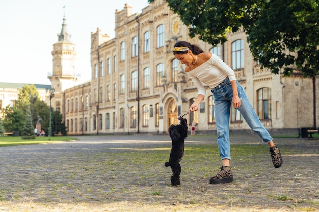 Счастливый владелец развлекается с молодой забавной собакой на улице Леди в стильной повседневной одежде