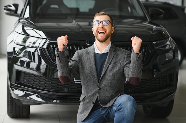 新しい車の幸せな所有者 カジュアルな服を着た感情的なハンサムな男は、ディーラーで車を買って幸せです