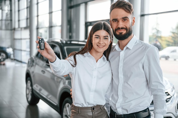 Foto proprietari felici l'uomo con la donna in abiti bianchi è insieme nella concessionaria dell'auto