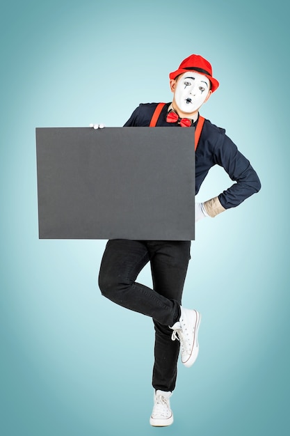 A happy pantomime man holds a black board on a blue background.