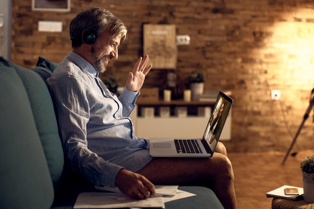 Happy pantsless businessman having video call over laptop in\
the evening at home