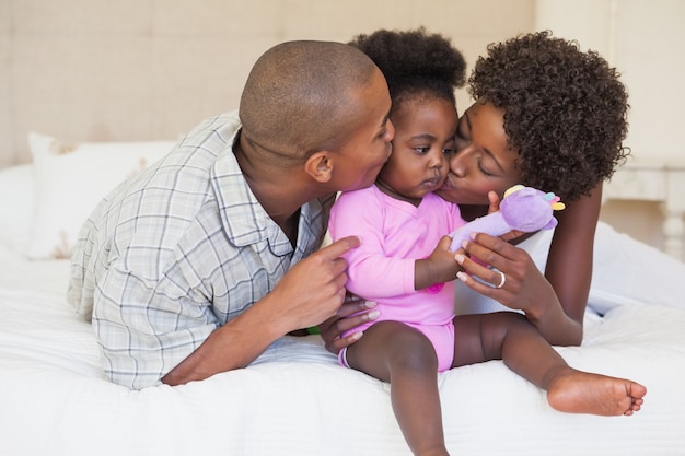 Happy parents and baby girl sitting on bed together