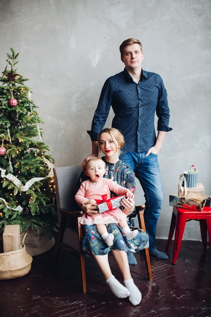 Happy parents and daughter posing near christmas tree.