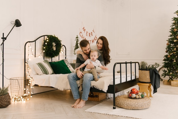 Happy parents play with baby on bed before Christmas