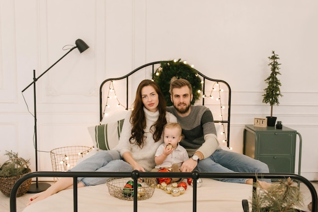 Happy parents play with baby on bed before Christmas