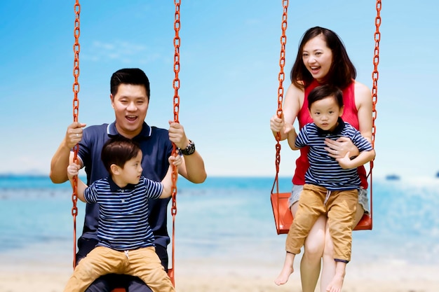 Happy parents playing swings with sons on beach