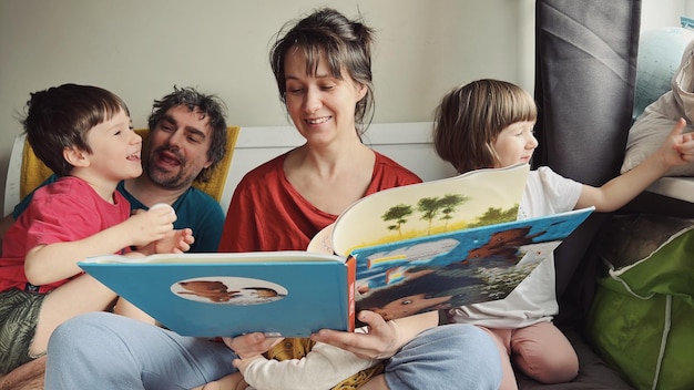 幸せな両親がベッドに座っている子供たちに本を読ませている