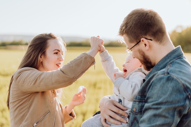 Happy parents spend time and play with their baby in the summer on a sunny day at sunset